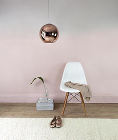 a white chair sitting in front of a pink wall with a mirror hanging above it