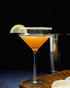 an orange cocktail in a coupe glass with a lemon wedge on the rim and a towel next to it