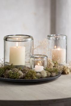 two glass jars filled with candles on top of a table next to moss and flowers