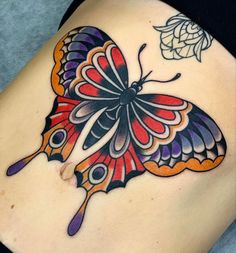 a colorful butterfly tattoo on the back of a woman's stomach, with an insect flying above it