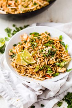 a white bowl filled with noodles and topped with lime wedges next to a skillet