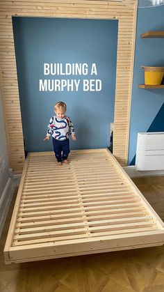 a young boy standing on top of a bed frame in a room with blue walls