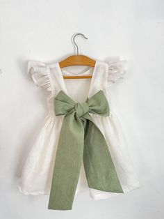 a white shirt with a green bow on it and a wooden hanger hanging from the wall