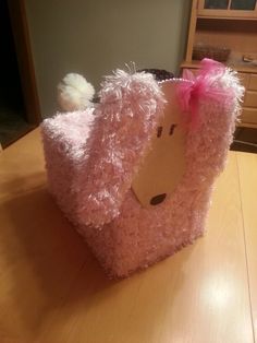 a pink stuffed animal with a bow on its head sitting on top of a wooden table