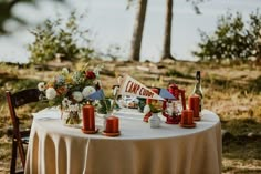 a table with candles and flowers on it in the middle of an open field next to some trees