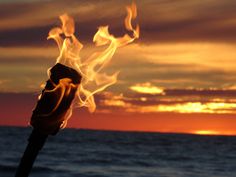 a fire stick with flames coming out of it near the ocean at sunset or sunrise