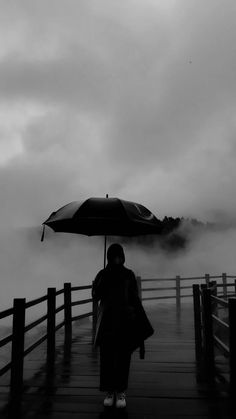 a person standing on a dock with an umbrella over their head, in the rain