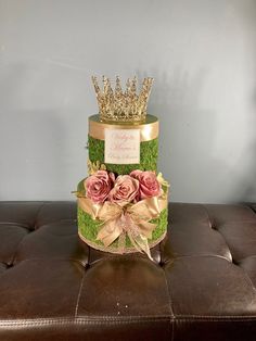 a green cake with pink roses and a gold crown on top is sitting on a brown ottoman