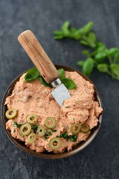 a bowl filled with hummus and pickles on top of a black table next to some green leaves