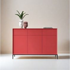 a red cabinet with two vases on top and a plant in the middle, against a white wall