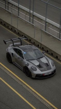 a silver sports car driving down a road next to a bridge with no cars on it