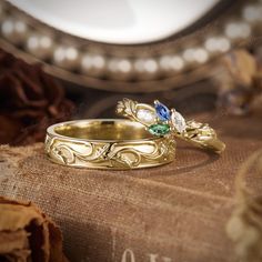 two gold wedding rings with blue and green stones sitting on top of an old book