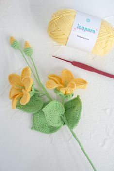 two crocheted flowers and yarn next to a pair of knitting needles on a white surface