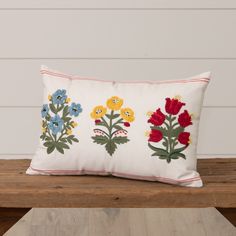 a white pillow with colorful flowers on it sitting on a wooden bench next to a wall