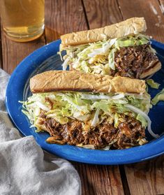 two pulled pork sandwiches on a blue plate next to a glass of beer and napkin