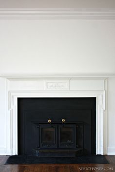 an empty fireplace in a white room with wood flooring and black painted mantel