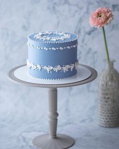 a blue and white cake sitting on top of a table next to a pink flower