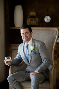 a man sitting in a chair holding a wine glass and wearing a suit with a flower on the lapel