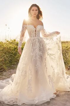 a woman in a wedding dress standing on the beach with her arms around her body