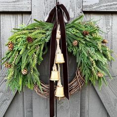 a wreath with bells hanging from it and evergreen leaves on the front door, next to a wooden fence