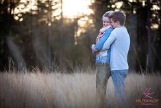 two people hugging each other in the middle of a field with trees in the background