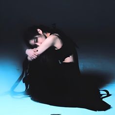 a woman sitting on the ground with her head in her hands, wearing a black dress