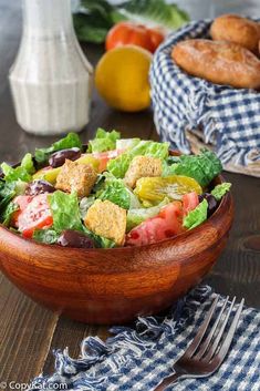 a salad in a wooden bowl on a table with other food items and utensils