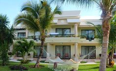 a hammock between two palm trees in front of a white building with balconies