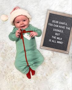 a baby wearing a santa hat laying next to a sign