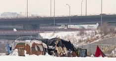 several tents are set up in the snow near an overpass and bridge with traffic