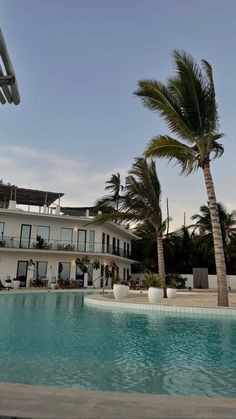 an empty swimming pool in front of a large white house with palm trees on the side