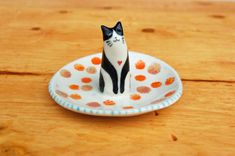 a small black and white cat sitting on top of a plate with polka dot designs