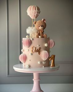 a pink cake decorated with balloons and a teddy bear sitting on top of the cake