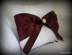 a white pillow with a red bow on it's side and a diamond brooch in the center