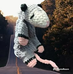 a crocheted stuffed animal hanging from the side of a road with trees in the background