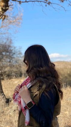 a woman standing in front of a tree with her back to the camera, wearing a jacket and scarf