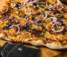 a pizza sitting on top of a wooden cutting board next to a knife and spatula