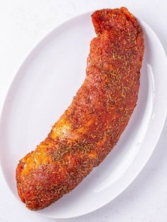 a piece of meat on a white plate with seasoning sprinkled around it