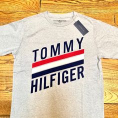 Tommy Hilfiger Grey Tee Size Youth Xl Fits Like A Junior Medium Grey With Blue Tommy Hilfiger Logo Emblazoned Goes Great With Matching Trackpants/Sweatpants And Hoodie Bundle! New With Tags Gray Logo Print T-shirt For Spring, Trendy Gray Tops With Logo Print, Tommy Hilfiger Blue Logo Print Tops, Tommy Hilfiger Spring Tops With Logo Print, Tommy Hilfiger Tops With Logo Print For Spring, Spring Tommy Hilfiger Tops With Logo Print, Tommy Hilfiger Casual Graphic Print Tops, Gray Logo Print Casual Shirt, Gray Casual Shirt With Logo Print