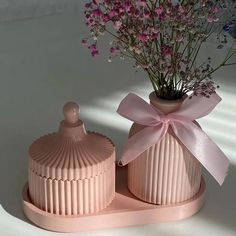 two pink vases with flowers in them on a white tableclothed surface, one has a pink bow and the other is made out of ribbedding