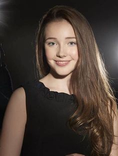 a woman with long brown hair standing in front of a camera and smiling at the camera