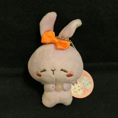 a small stuffed animal with an orange bow on its head and ears, sitting against a black background