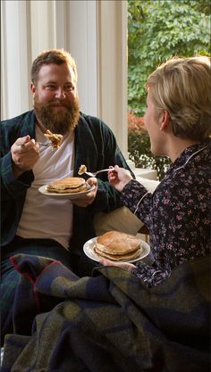 a man and woman sitting on a couch eating pancakes