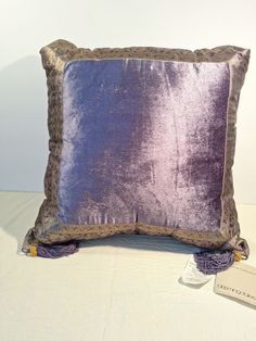 a purple and gold pillow sitting on top of a white table next to a tag