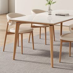 a dining table with four chairs and a vase on the top, in front of a white wall