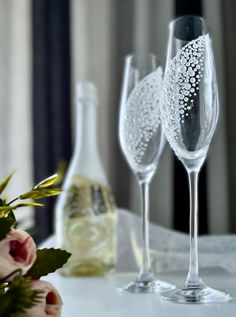 two wine glasses sitting on top of a table next to bottles and flowers in vases