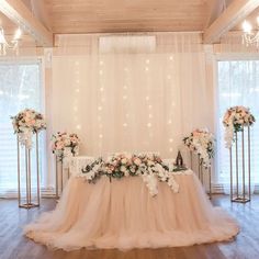 a table with flowers and candles on it in front of a white curtained backdrop