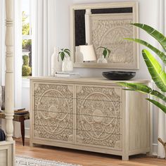 a white dresser sitting next to a plant in a living room