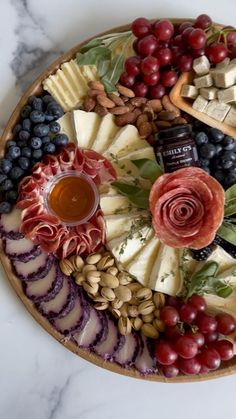 a platter filled with cheese, grapes, nuts and other foods on top of a marble counter