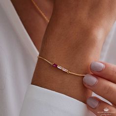 a woman's hand wearing a gold bracelet with an amethorate bead